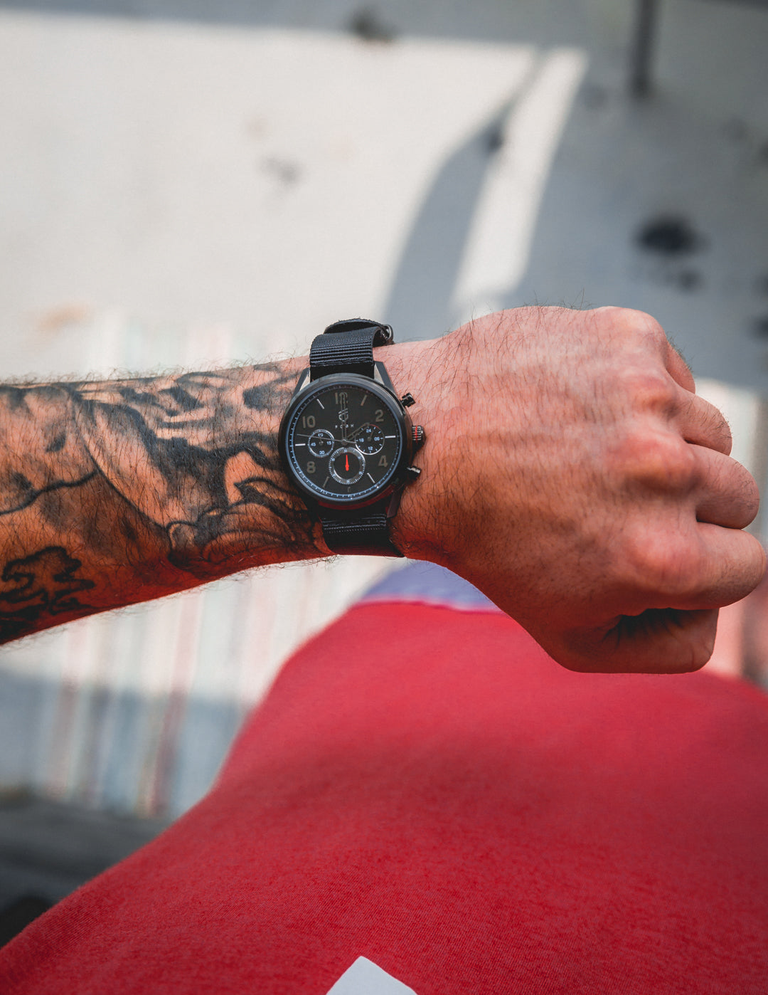 Tattooed men's arm with black watch and red shirt   