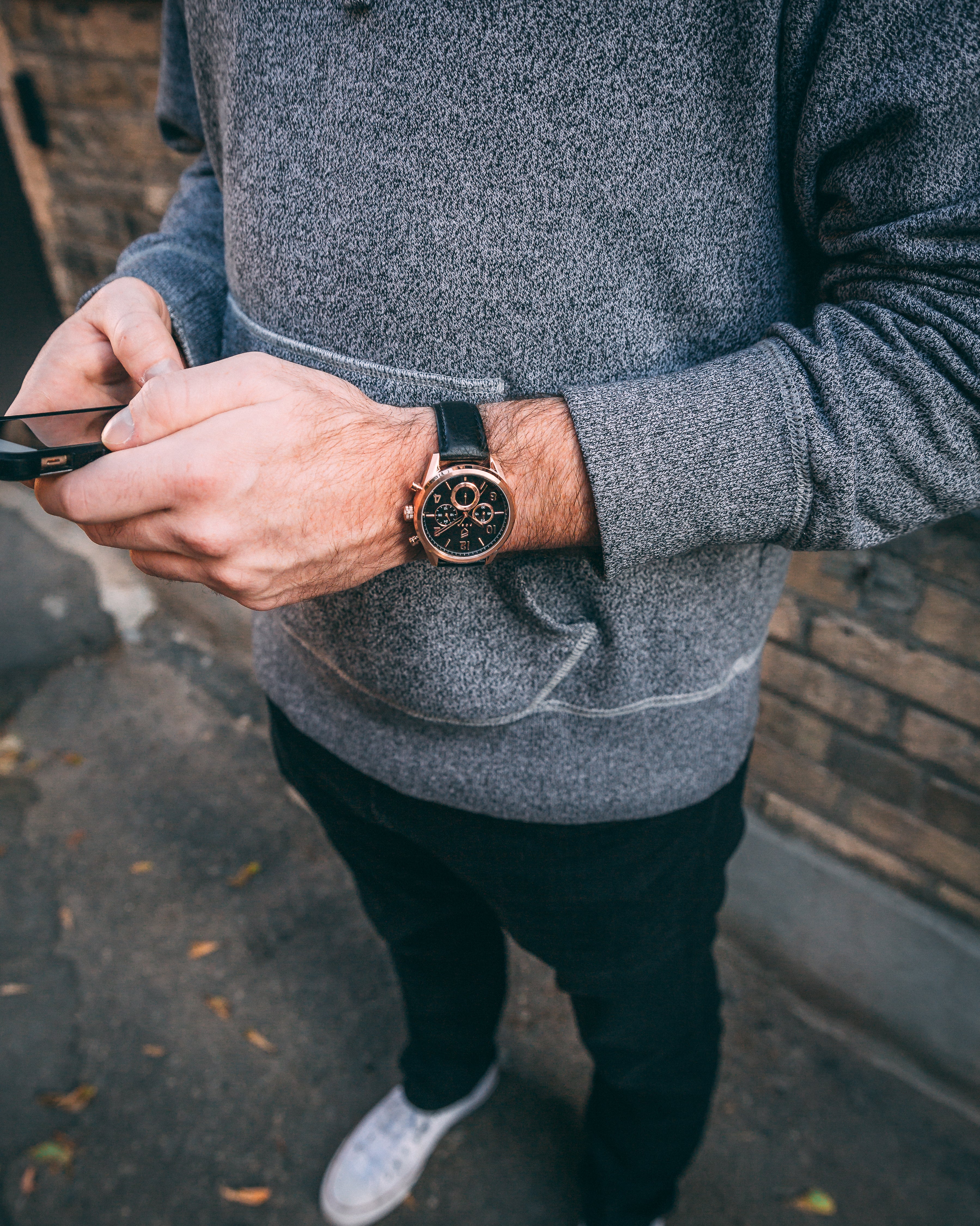 man on phone with grey hoodie and white converse with rose gold watch 