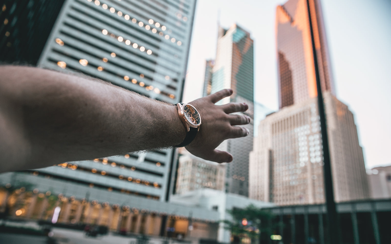 hand with rose gold watch pointing to city skyline view in Toronto Canada