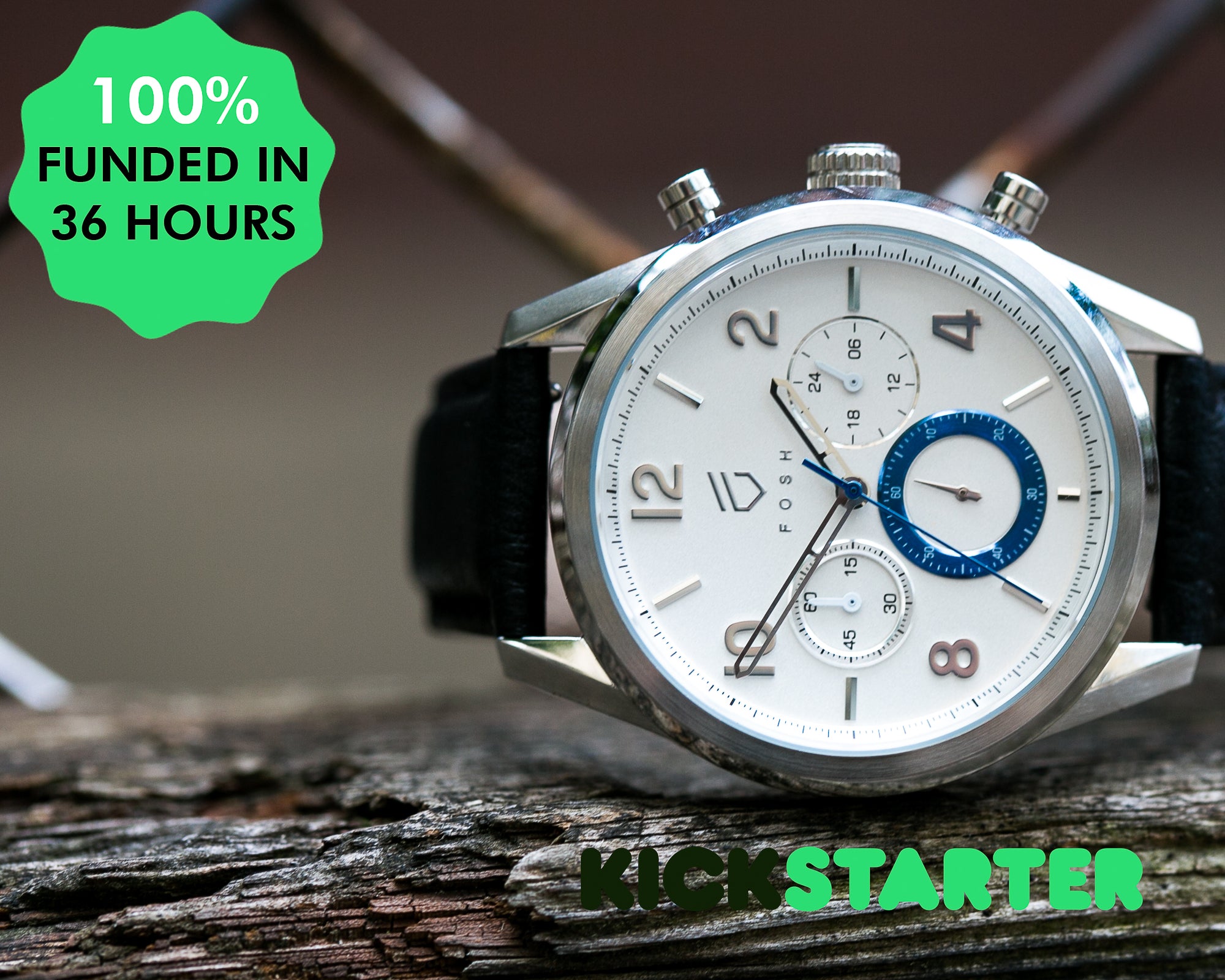 Stainless steel watch with white face and blue second hand on distressed wood with 100% funded on kickstarter sticker