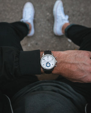 man in black bomber jacket and white converse with silver and blue chronograph watch 